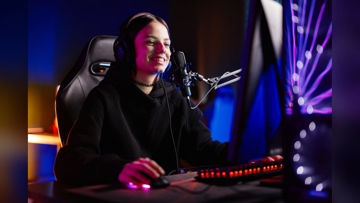 Smiling streamer in headphones speaking into a boom-arm microphone at a gaming desk with an RGB-lit keyboard