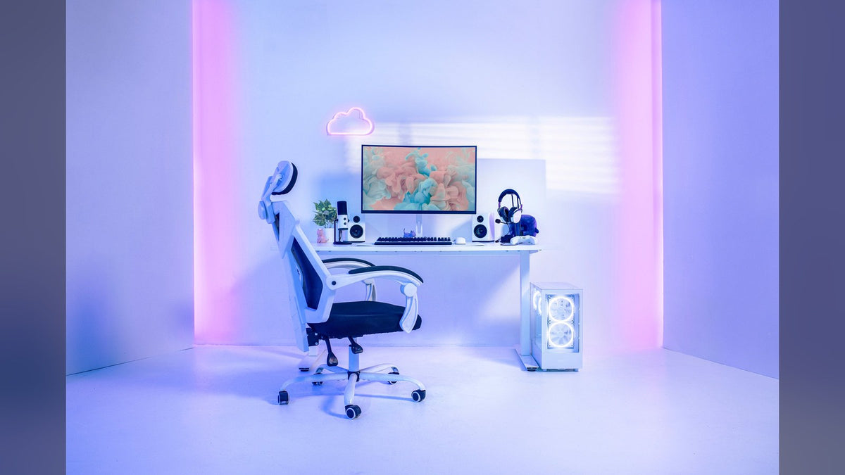 White gaming desk setup with a mesh office chair, monitor, headset, cloud neon sign, and a white PC with RGB fans