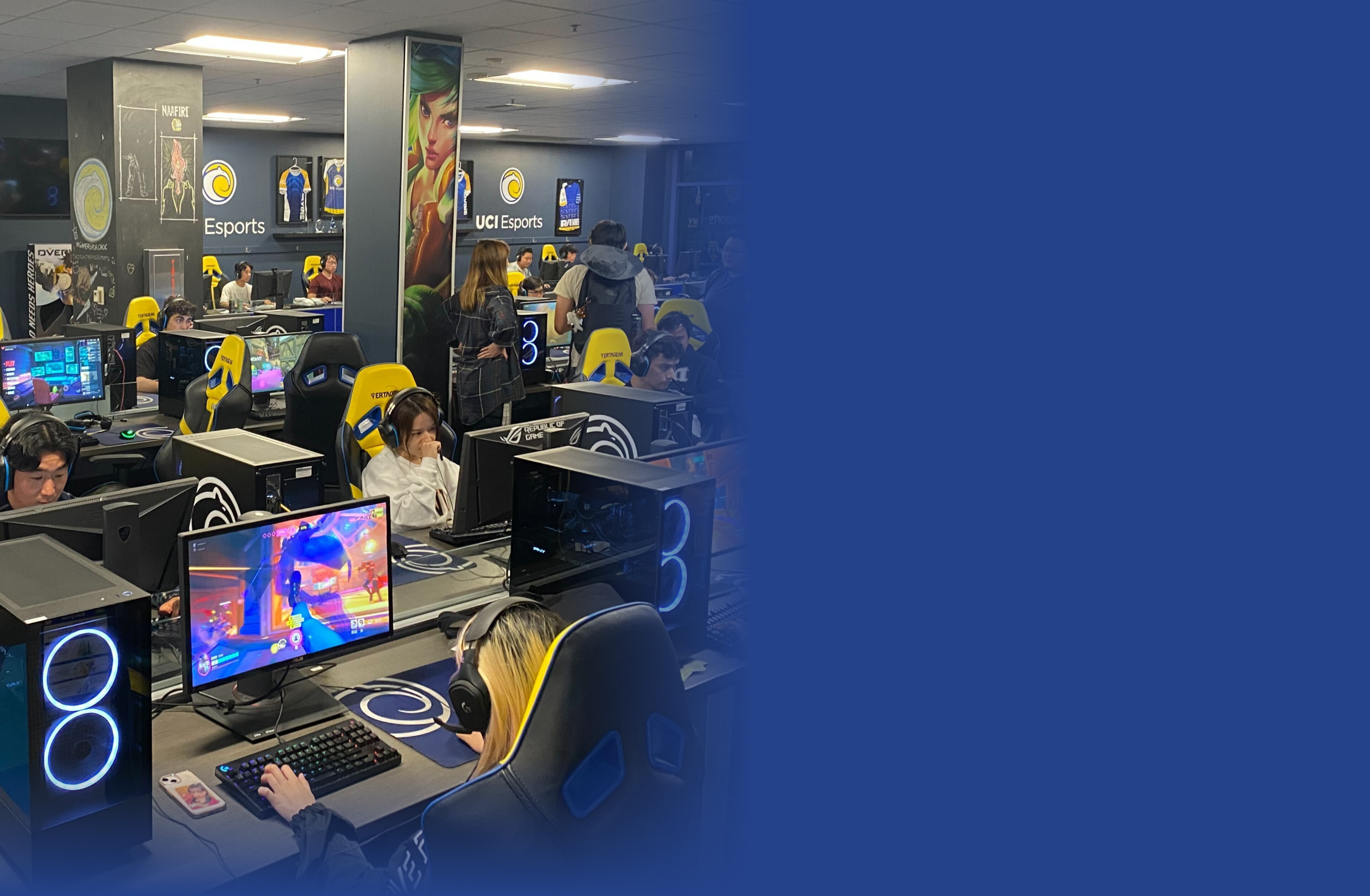 Students sit at gaming computers in a modern esports room, wearing headphones and focused on screens. UCF Esports logos and posters are visible on the walls. Some people stand and observe. The right side is a blue fade.