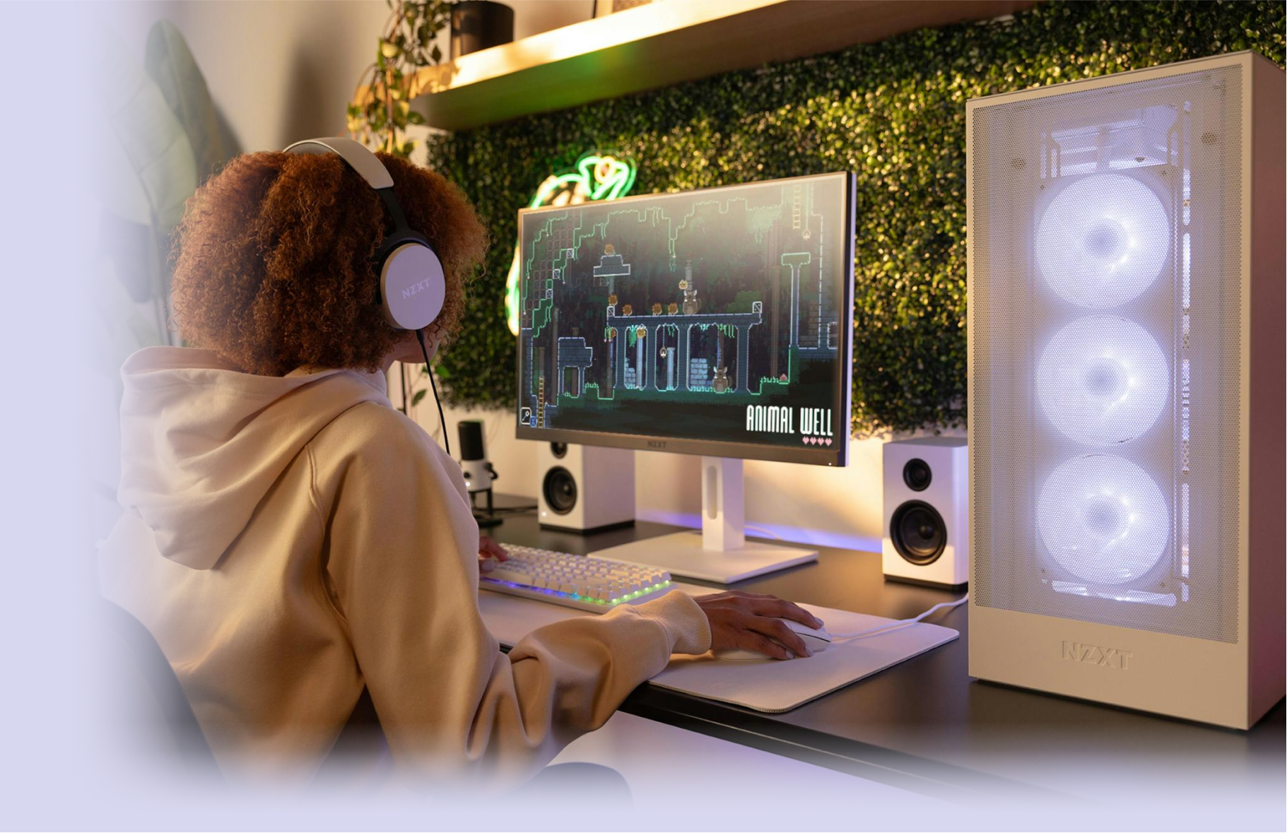 A person wearing headphones sits at a desk, playing the game Animal Well on a monitor. A glowing white PC tower with three fans is beside the monitor, and the setup is surrounded by greenery and LED lighting.