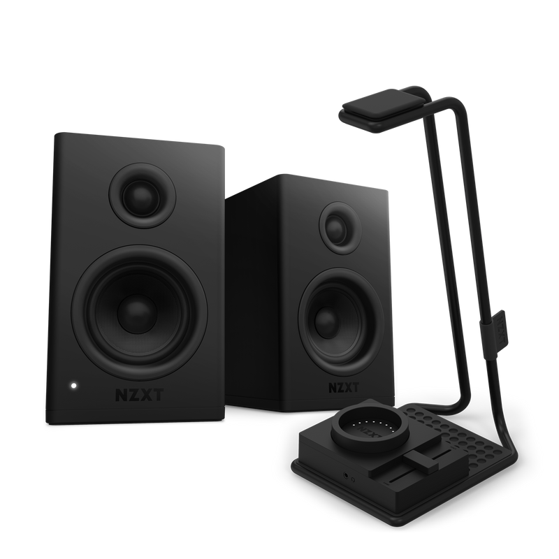 Two black NZXT Relay Speakers + SwitchMix with circular drivers are placed beside a sleek black desk organizer with a lamp and wireless charging pad, delivering high-resolution audio against a dark background.